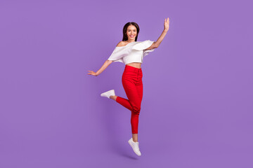 Photo of cheerful sportive lady jump raise arm wear white blouse trousers footwear isolated purple color background