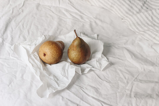 Couple of yellow pear fruit on crinckled wrapping paper. Autumn, summer breakfast in bed composition.White striped linen bedding. Feminine lifestyle composition. Rustic interior. Copy space.