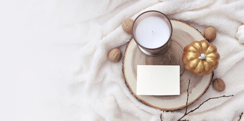 Mock autumn or winter scene. Empty greeting card, candle and decorative pumpkin on white  plaid....