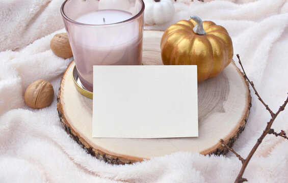 Mockup empty paper blank, aroma candle and gold pumpkin on white plaid. Autumn still life composition. Cozy fall decor for wedding invitation card, business. Eco home details interior. Hygge.