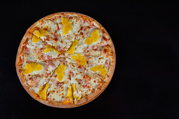 Hawaiian pizza topped with pineapple with chicken on mozzarella cheese on a thick pie crust on a black background