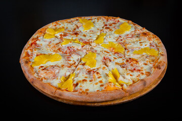 Hawaiian pizza topped with pineapple with chicken on mozzarella cheese on a thick pie crust on a black background