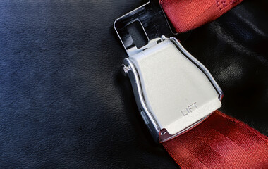 Red lap belt of an empty seat inside an airplane with the word LIFT embossed on the metal