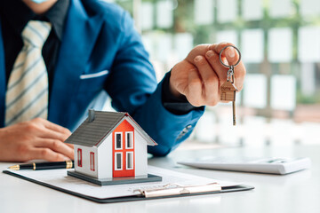 Real Estate Broker Or businessman holding white house model and house key in hand.Mortgage loan approval home loan and insurance concept.