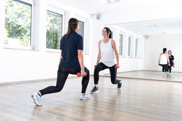Zwei junge Frauen machen Sport in einer Sporthalle mit Spiegel, Physiotherapie, Bewegungstherapie