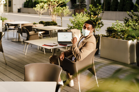 Young Black Man In Face Mask Working With Laptop At Cafe