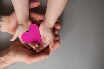 male and child's hands are holding a pink heart. world heart day, world health day, world family day
