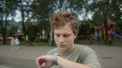 Young blond colored-eyed boy looks at his wristwatch and conveys that the time is too late, looks...