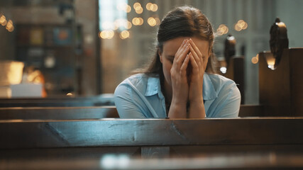 Woman is sitting in a church and praying. - obrazy, fototapety, plakaty