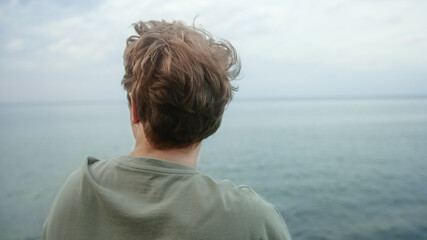Young handsome blond boy puts his hands behind his neck and looks towards the horizon, deep in...