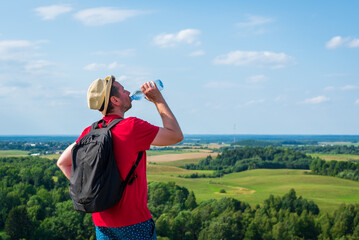 Traveler drinks water in the mountains.Hiker with backpack relaxing on top of the mountain in summer sunny day.
