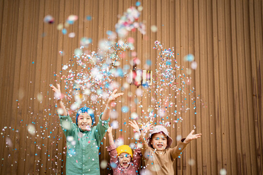 Happy children throwing confetti in front of brown wall