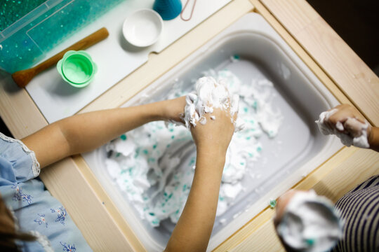 children play with water beads and shaving foam; child with dirty hands makes ice cream from foam. Sensory boxes and development. Montessori classes at home