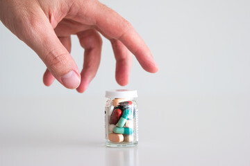 Caucasian male hand reaching out for a glass bottle full of various colored medical pills, tablets and capsules. Close up studio shot, isolated on white background