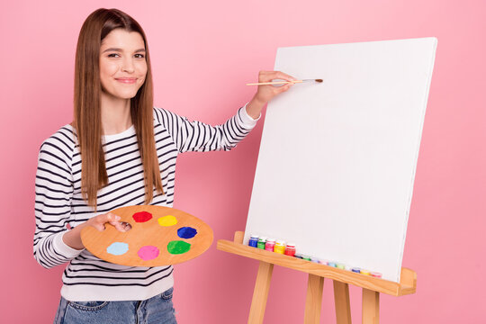 Portrait of attractive cheerful talented girl making new painting picture isolated over pink pastel color background