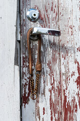 An old door with a newer lock and a handle. The paint is badly chipped, there is part missing from the door frame and an abandoned dog-collar is hanging from the door handle. 
