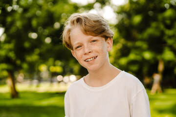 Ginger white boy wearing t-shirt smiling while standing in green park