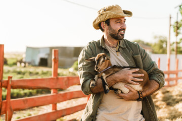 White man smiling and holding goat while standing on farm © Drobot Dean