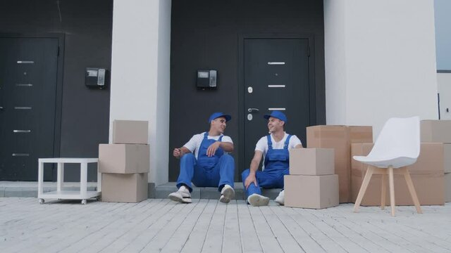 Two removal company workers have a break while sitting on the step