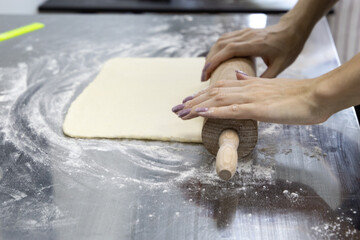 The process of rolling out puff pastry with multiple layers on a table with flour and a rolling pin. Workpiece for pastry and croissants