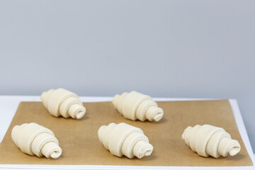 Fototapeta na wymiar Croissants formed from raw dough lie on baking paper before being sent to the oven. Handmade pastry baking process