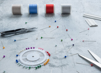Basting pins with colored heads on a white concrete surface, a sewing ripper, chalk for cutting,...