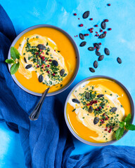 Pumpkin carrot soup and seeds, with cream, and parsley on a blue wooden background and blue napkin....