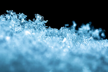 Natural snow texture with snowflakes close-up in soft blue tones on the window, isolated on black background with space for text. Blank for holiday gift cards. Macro texture of snow.