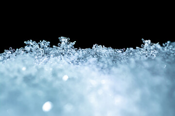 Natural snow texture with snowflakes close-up in soft blue tones on the window, isolated on black background with space for text. Blank for holiday gift cards. Macro texture of snow.