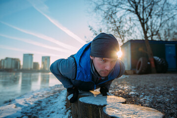 A man is engaged in functional training in winter in very cold and clear weather. push-ups from the floor. on the background of the city