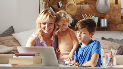Happy family at home, mother with son and daughter have fun using computer, smiling parent with children surfing internet on laptop, sitting comfortably in living room communicate remotely with father