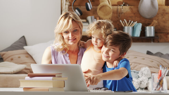 Happy Family At Home, Mother With Son And Daughter Have Fun Using Computer, Parent With Children Browsing Internet On Laptop, Child Student Shows Something Pointing At The Monitor