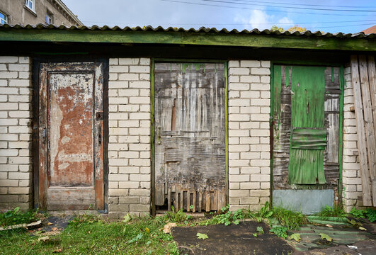 Three very old barn doors made of rough textured hardly weathered old plywood. Green grass in front of. Barn made of white brick.