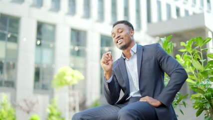 african american business man smoking cannabis outdoors sitting on city park bench on urban street background. Male employee Businessman. Office worker in suit Relieves stress a marijuana outside