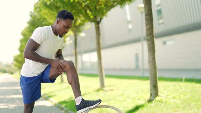 young african american runner athlete with muscle pain. Man massaging Stretching, trauma injury while jogging outdoors. Fitness male sprain severe pain stretch pull. Leg muscle cramp calf sport