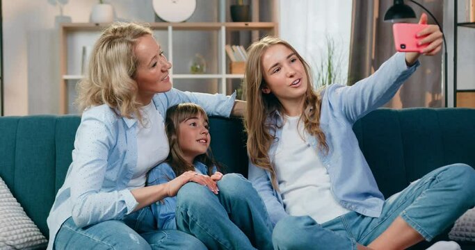 Family concept where attractive positive carefree happy friendly woman and her daughters enjoying video call with relatives on mobile at home,front view