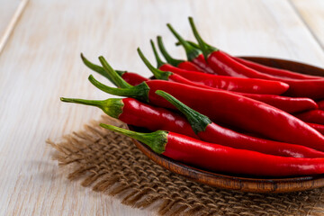 Cropped image of red hot chili peppers with green tales on a brown wooden saucer over rustic table. Front view of fresh spicy chile cayenne peppers ready for cooking. Ingredient for spicy dishes.