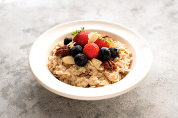 Oatmeal porridge with fresh berries blueberry and strawberries in white bowl on grey background.