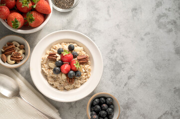 Oatmeal porridge with fresh berries blueberry and strawberries in white bowl on grey background.