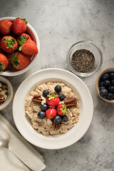 Oatmeal porridge with fresh berries blueberry and strawberries in white bowl on grey background.