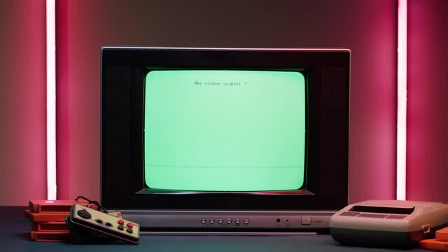Old television with blue screen on red neon background. Close-up of vintage tv and retro playstation, changing cartridges. Antique video game, nostalgia. 