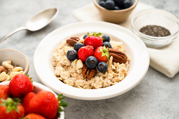 Oatmeal porridge with fresh berries blueberry and strawberries in white bowl on grey background.