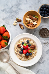 Oatmeal porridge with fresh berries blueberry and strawberries in white bowl on grey background.
