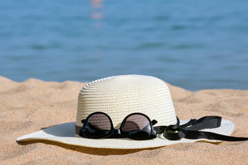 Closeup of yellow straw hat and black protective sunglasses on sandy beach at tropical seaside on warm sunny day. Summer vacation concept.