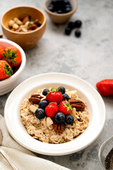 Oatmeal porridge with fresh berries blueberry and strawberries in white bowl on grey background.