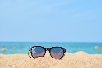 Fototapeta na wymiar Closeup of black protective sunglasses on sandy beach at tropical seaside on warm sunny day. Summer vacation concept.