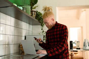 Albino african american man with dreadlocks working from home and using laptop and smartphone