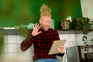 Happy albino african american man with dreadlocks making video call and using tablet
