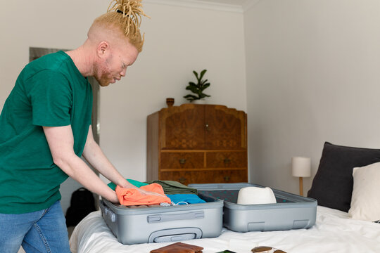 Albino african american man packing suitcase in bedroom - Powered by Adobe