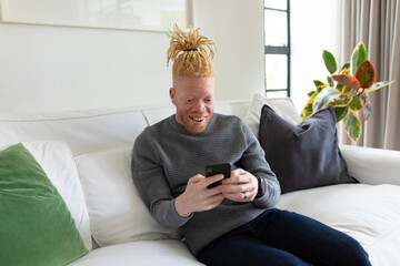 Happy albino african american man in the living room using smartphone